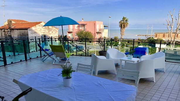 A terrace with a table and chairs, a blue umbrella, and a view of the sea. - Terrace overlooking the sea and Marche hills (Grottammare)