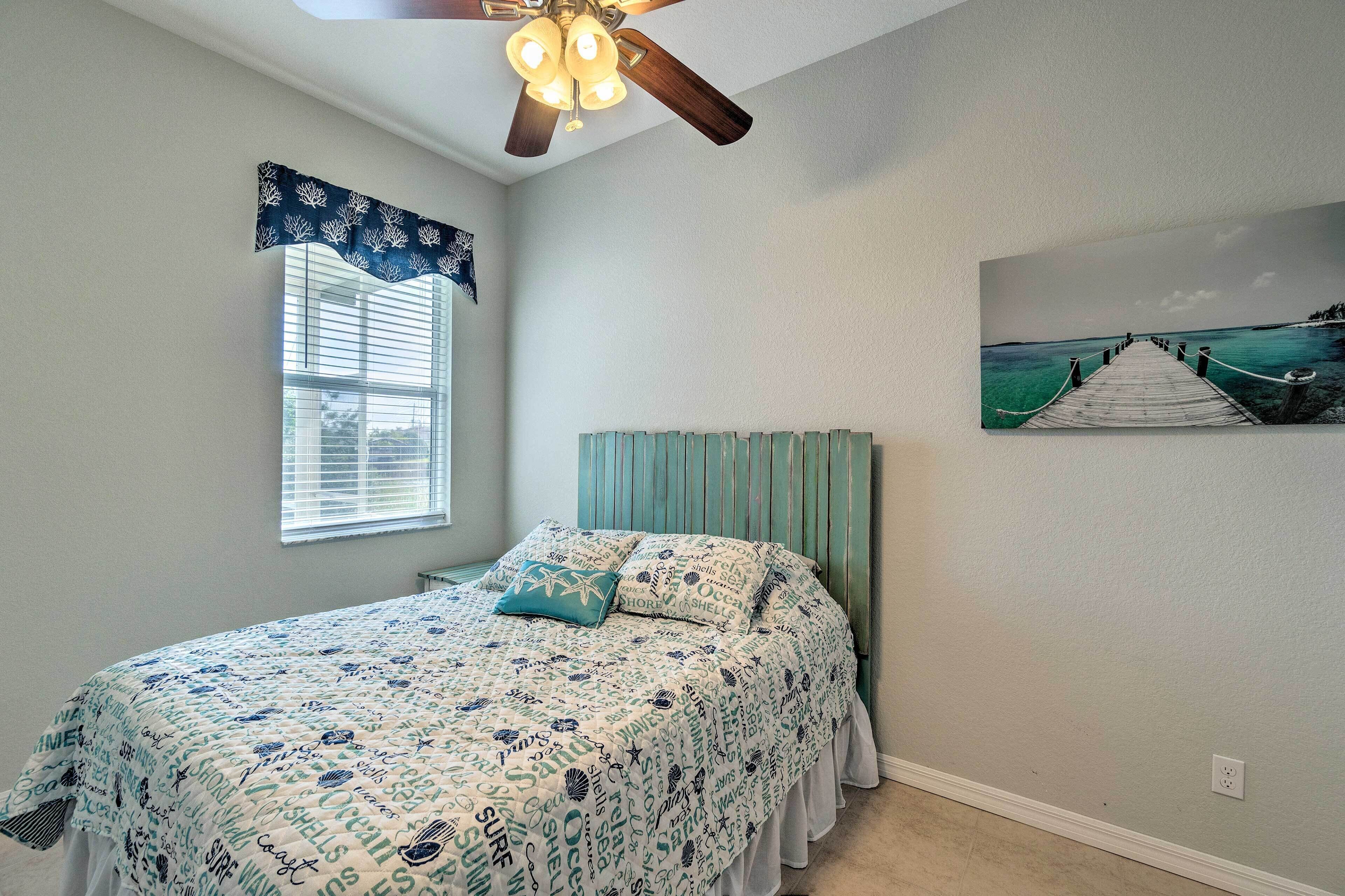 A bedroom with a bed, a ceiling fan, a window with blinds, and a painting of a pier.