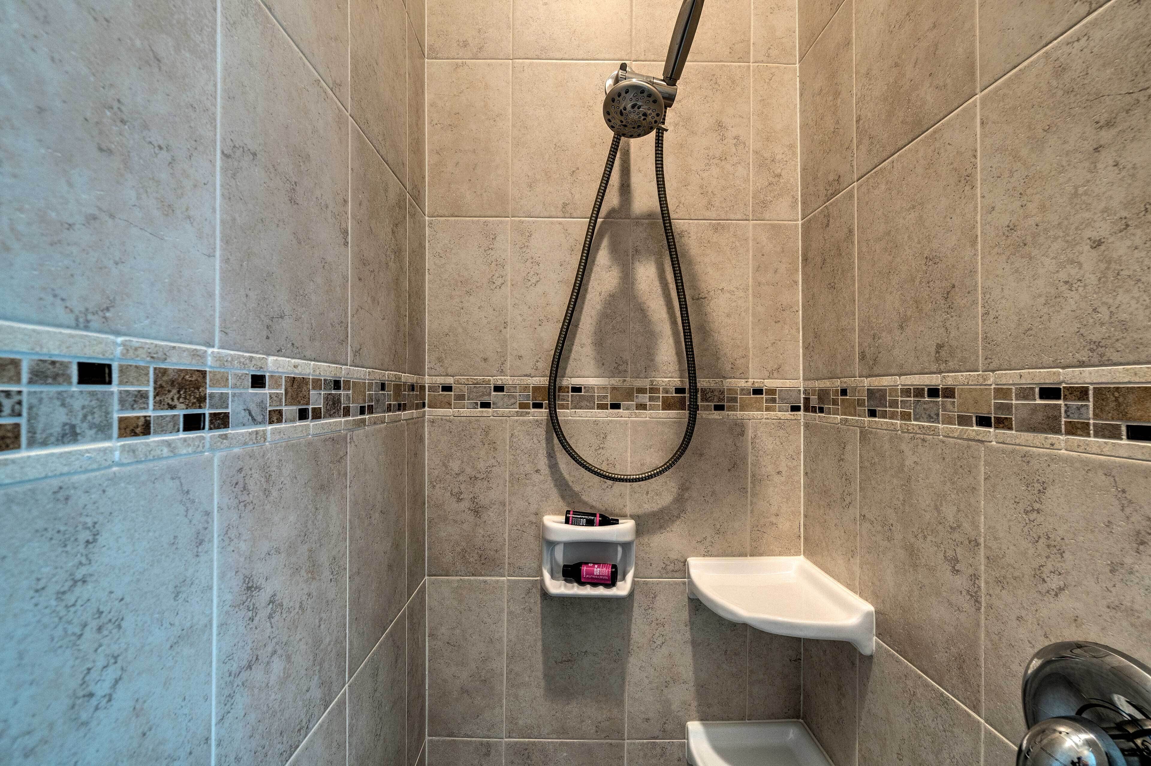 Ein Duschbereich mit Handbrause, einer kleinen Ablage für Toilettenartikel und einem weißen Waschbecken.