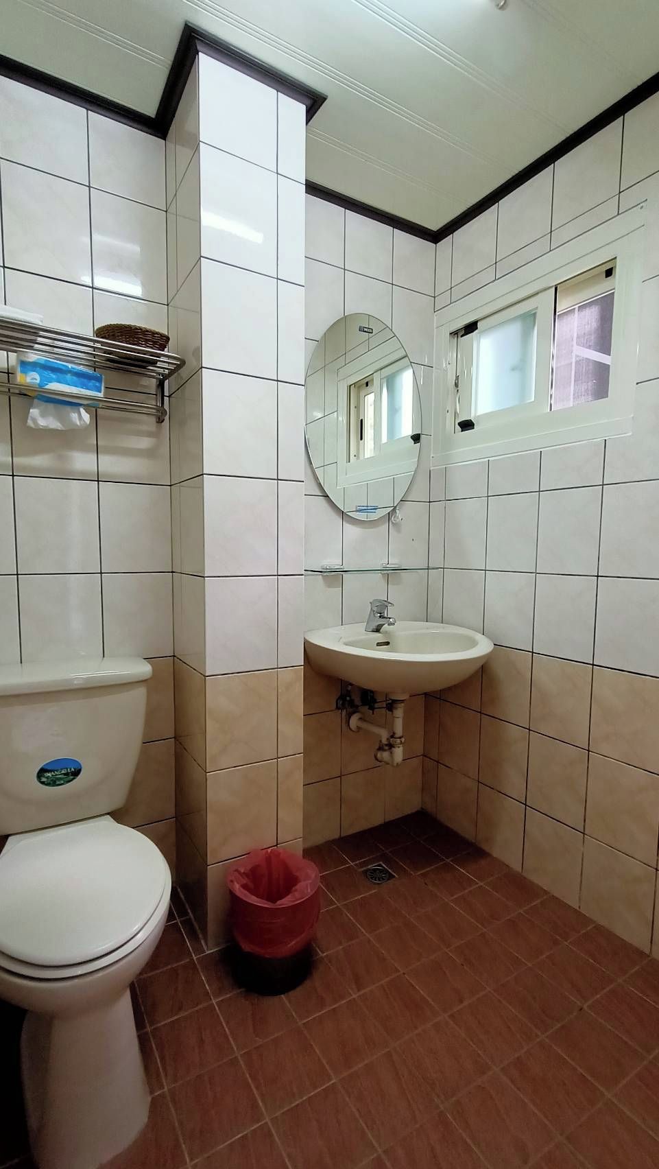 A bathroom with a toilet, sink, mirror, and tiled walls.
