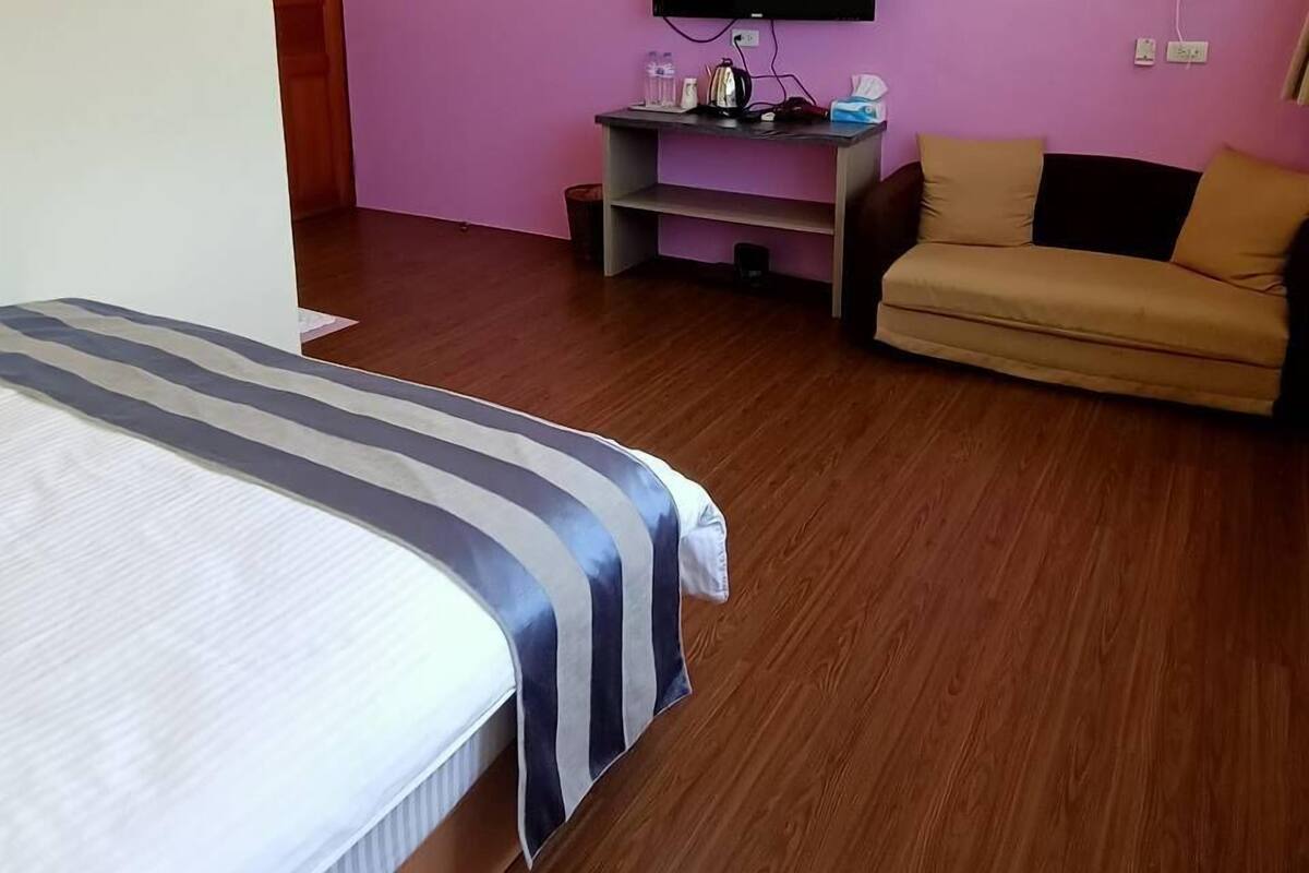 A modern hotel room with a bed, a sofa, a TV, and an air conditioning unit on the wall.