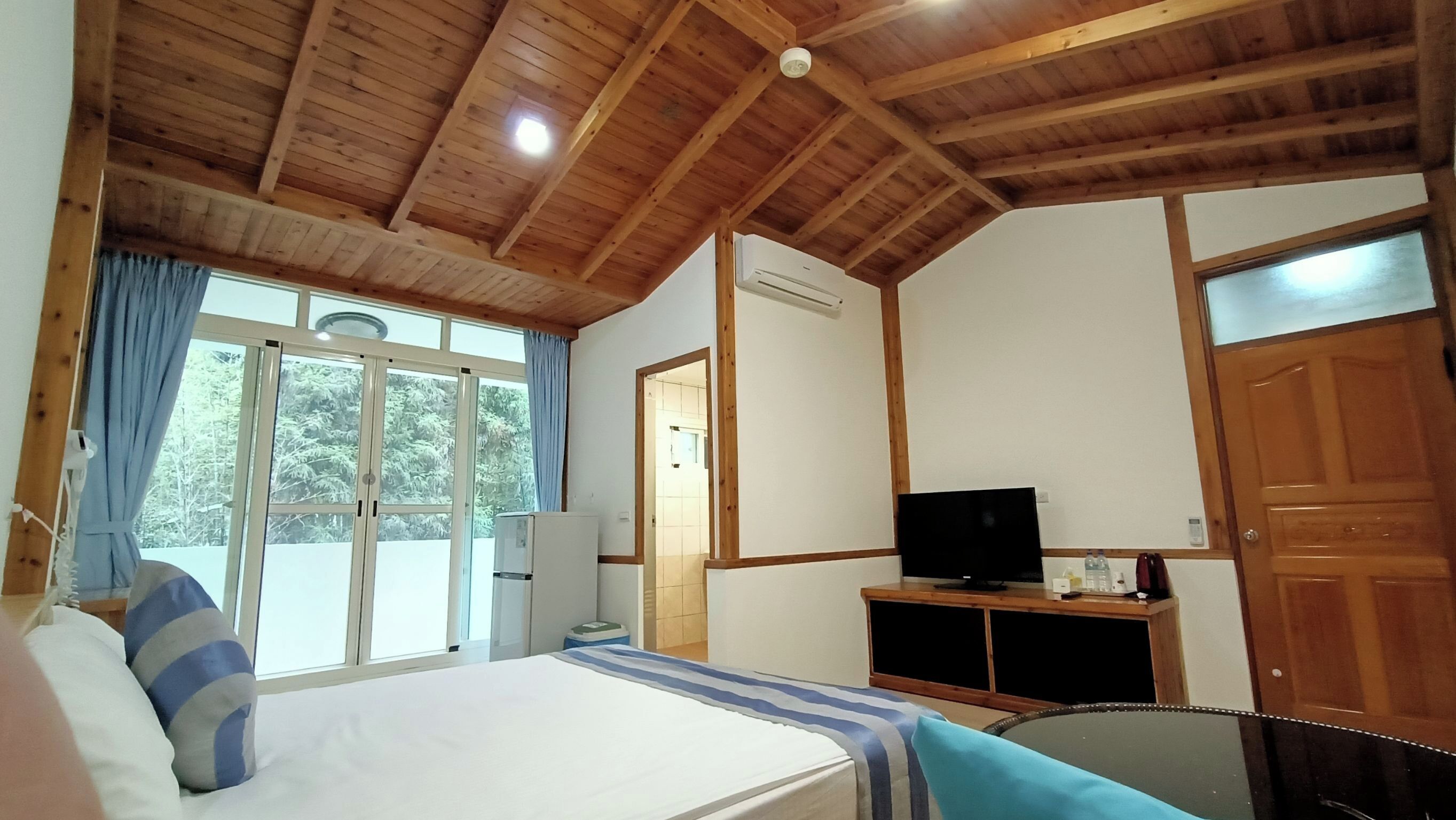 A bedroom with a bed, a television, and a sliding glass door leading to a balcony.