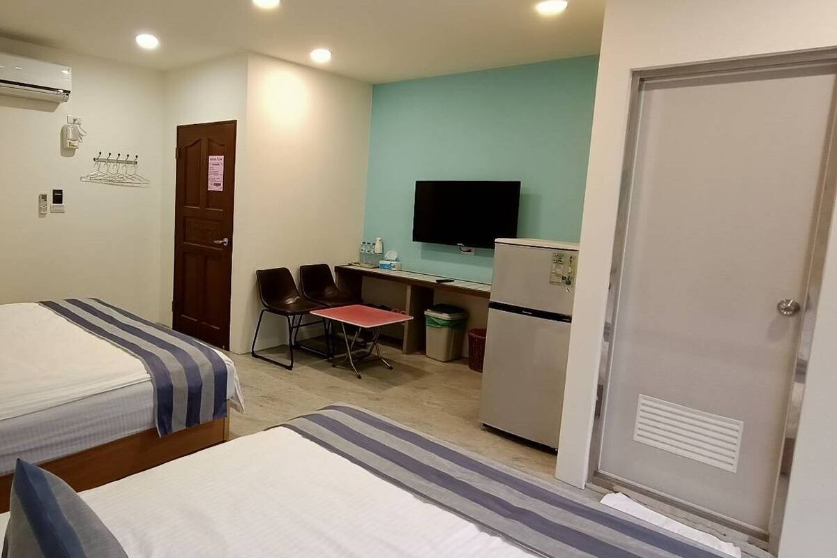 A hotel room with two beds, a desk, a chair, a TV, and a minibar.