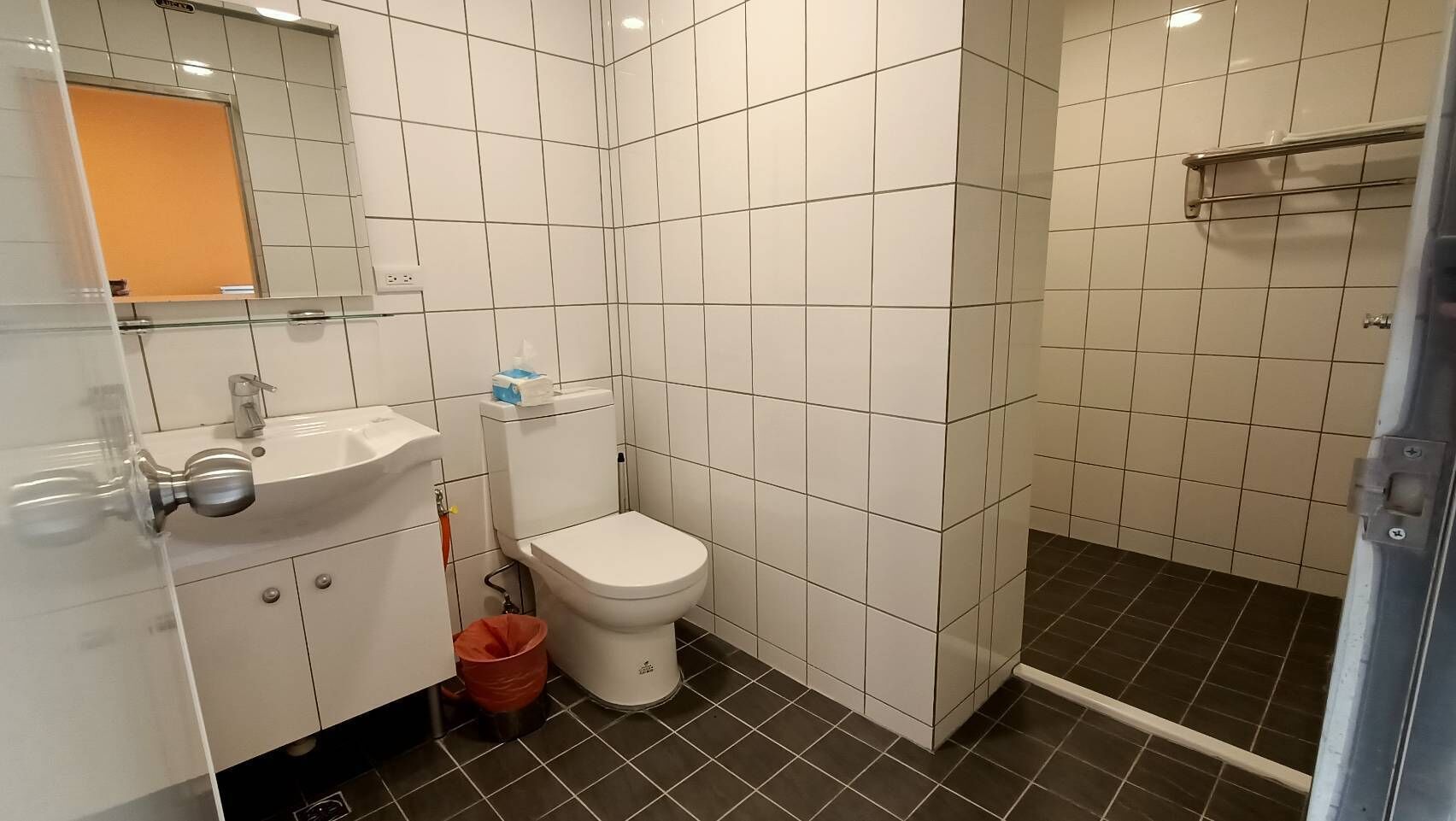Un baño con azulejos blancos, un lavamanos blanco, un inodoro y una zona de ducha.