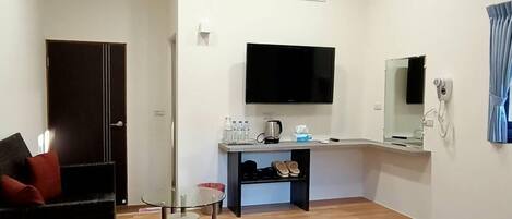 Habitación de hotel con techo de madera, televisor de pantalla plana, aire acondicionado, escritorio con silla, cama con ropa de cama estampada y una puerta.