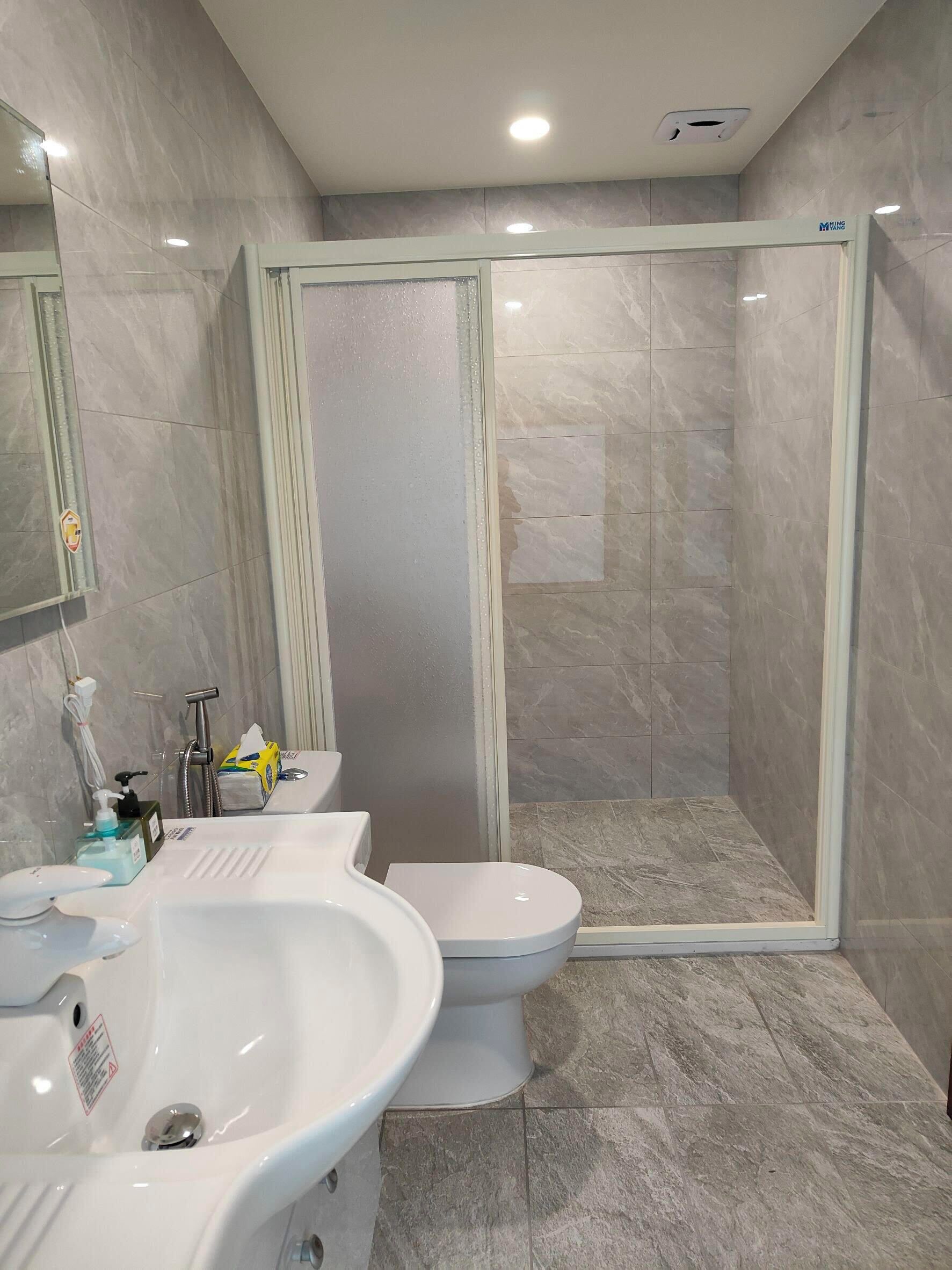 A modern bathroom with a glass-enclosed shower, a white sink, and a toilet.