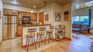 A modern kitchen with wooden cabinets, stainless steel appliances, and a bar area with stools. - Cozy Condo with Balcony, Walk to Shops, Dining, and Hot Springs Nearby! (Pagosa Springs)