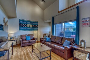 A spacious living room with leather sofas, a coffee table, and a large window offering a view of a mountain.