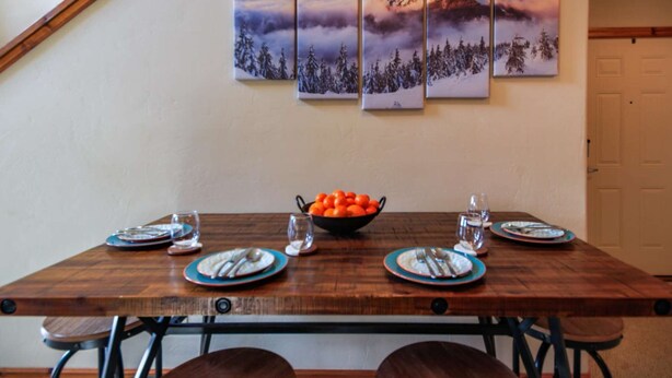 A dining table set with plates, cutlery, and a bowl of oranges. - Cozy Condo with Balcony, Walk to Shops, Dining, and Hot Springs Nearby! (Pagosa Springs)