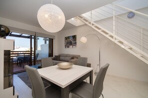 A modern living room with a dining table, grey sofa, and a large white pendant light.