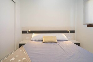 A neatly made bed with a headboard, two bedside tables, and a wall-mounted light fixture.