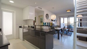 Una cocina moderna con una isla central, armarios blancos y un comedor con mesa y sillas.