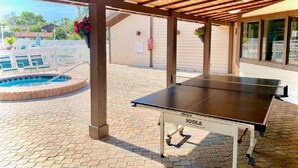 Ein Außenpoolbereich mit Tischtennisplatte, Whirlpool und überdachter Sitzgruppe mit Pergola.