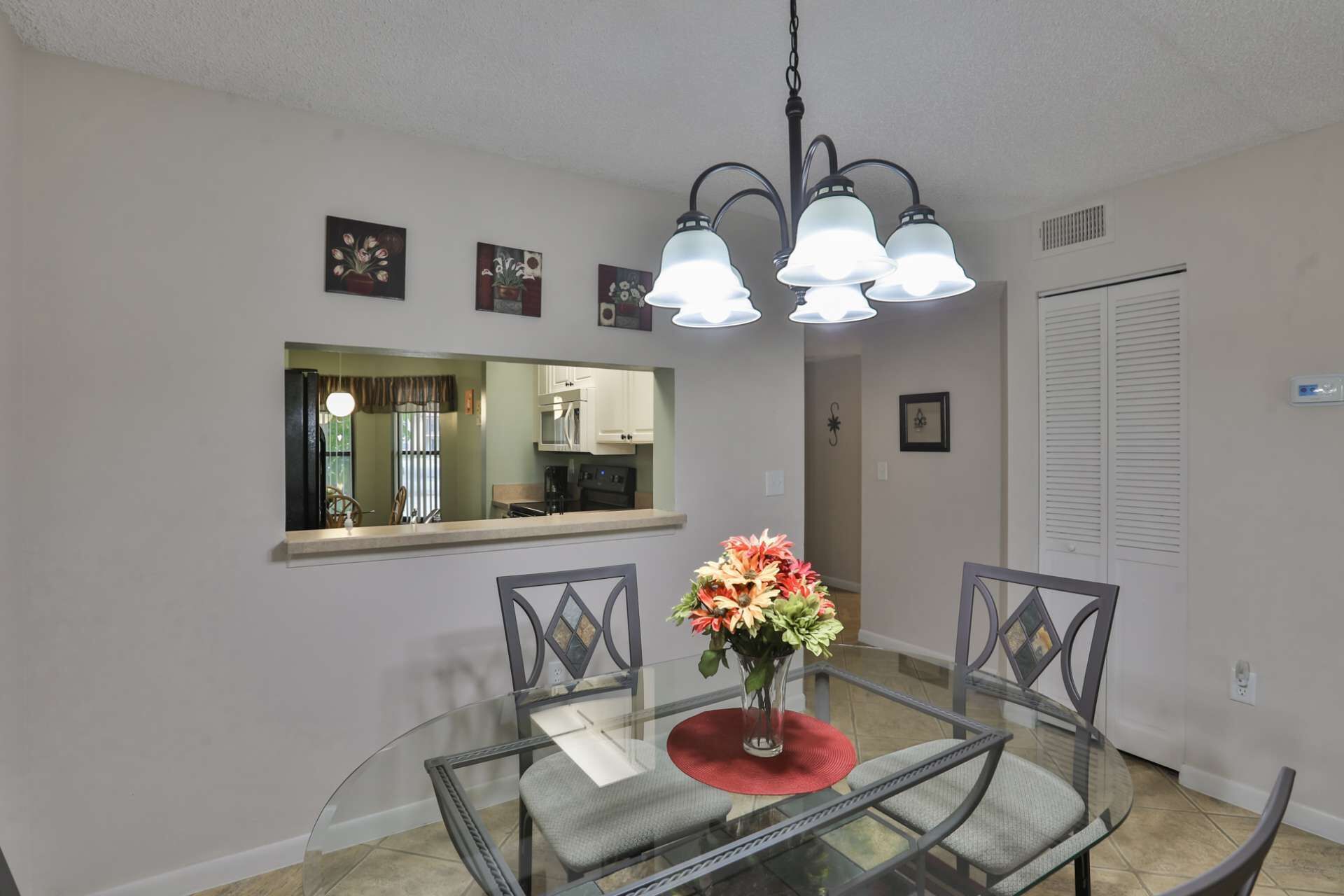 A dining area with a glass table, two chairs, a vase of flowers, and a hanging light fixture.