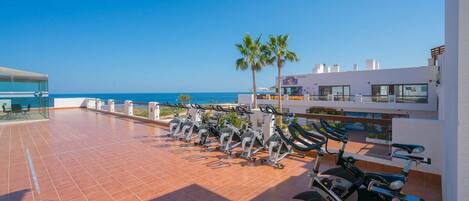 Un gimnasio en la azotea con bicicletas estáticas y vista al mar.