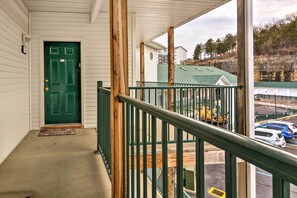 Step outside to a covered porch with a green door, wooden railing, and concrete floor.