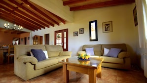 A living room with two sofas, a glass coffee table, wooden beams on the ceiling, and a tiled floor. - 44380 Finca Pula Viñas (Son Servera)