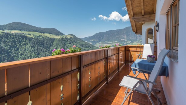 A balcony with a wooden railing, a table with a blue tablecloth, and a chair.