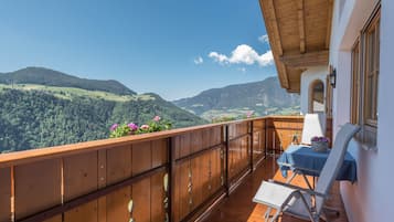 Ein Balkon mit Holzgeländer, einem Tisch mit blauer Tischdecke und einem Stuhl.
