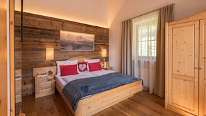 A wooden-framed bedroom with a bed, nightstands, a wardrobe, and a large window with curtains.