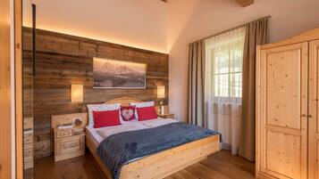 Ein Schlafzimmer mit Holzbettrahmen, einem Bett, Nachttischen, einem Kleiderschrank und einem großen Fenster mit Vorhängen.