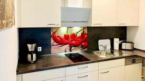 Una cocina moderna con armarios blancos, horno empotrado, cafetera y pileta.