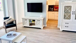 Un salón con televisor, un mueble blanco y una silla con almohadón.