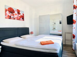 A hotel room with a large bed, a bedside table, a mirror, a TV, and a painting on the wall.