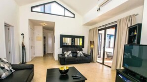 A living room with a sofa, a coffee table, a TV, a large mirror, and a sliding glass door leading to an outdoor area. - Casa Carra - Island Escape by Villas Now (Playa Blanca)