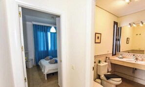 Une chambre avec un lit, une salle de bain avec un lavabo et un miroir, et un couloir.