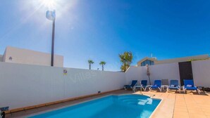 A swimming pool with blue lounge chairs, a clear sky, and a building with a white wall. - Casa Carra - Island Escape by Villas Now (Playa Blanca)