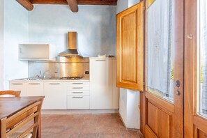 Una cocina con armarios blancos, una campana extractora de acero inoxidable y una puerta de madera con un ventanal.