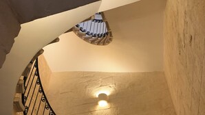 Una scala a chiocciola con ringhiera in ferro battuto e un punto luce fissato al muro.