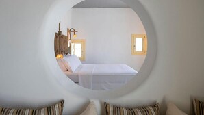 A circular window view of a bedroom with a bed, pillows, a hanging light fixture, and two wall-mounted lamps. - Pangaia Seaside Hotel Adults Only (Naxos)