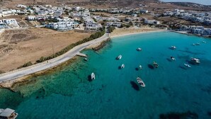 An aerial view of a coastal town with white buildings, a clear blue sea, and boats anchored near the shore. - Pangaia Seaside Hotel Adults Only (Naxos)