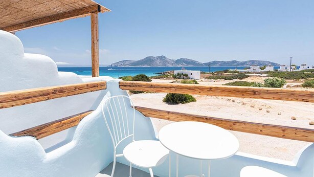 A beachside terrace with white chairs and tables, overlooking a clear blue sea and distant mountains. - Pangaia Seaside Hotel Adults Only (Naxos)