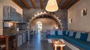 A modern interior with a kitchen, dining area, and a cozy seating area with a stone archway. - Pangaia Seaside Hotel Adults Only (Naxos)