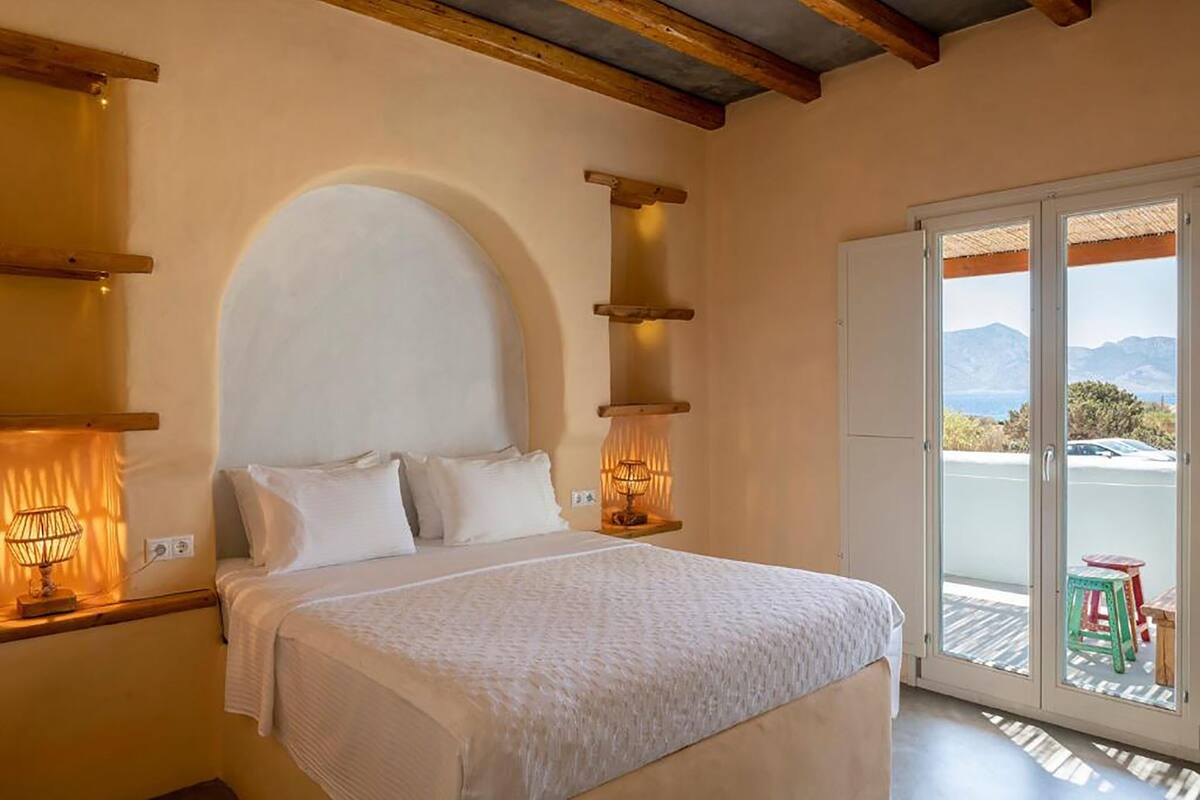 A bedroom with a large bed, a wooden headboard, and a view through a glass door to the outside.