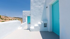 A narrow, white-walled corridor with turquoise doors and a small window, leading to a scenic landscape. - Pangaia Seaside Hotel Adults Only (Naxos)