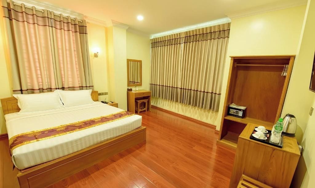 A hotel room with a bed, bedside table, mirror, wardrobe, and a window with curtains.
