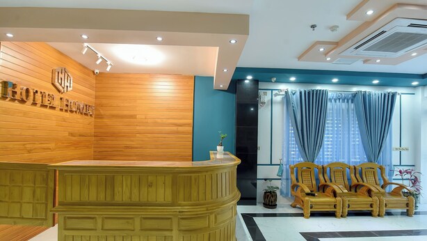 Zona de recepción de un hotel con un mostrador de madera, un espacio de estar con sillas y un amplio ventanal con cortinas.