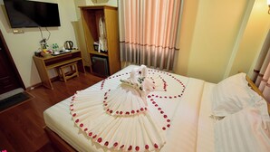 Habitación de hotel con una cama bien hecha, un televisor montado en la pared, un armario y un escritorio con varios objetos.