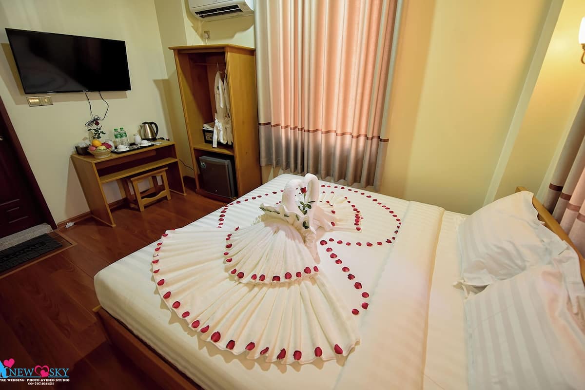 A hotel room with a neatly made bed, a television mounted on the wall, a wardrobe, and a desk with various items.