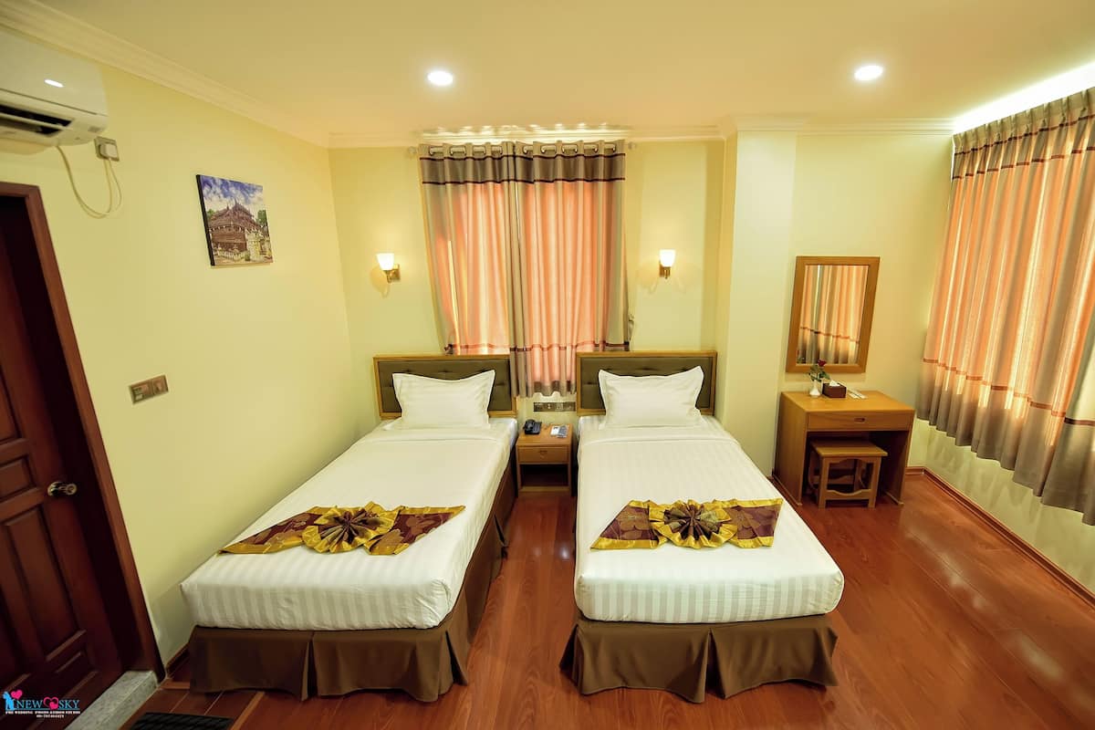 A hotel room with two single beds, a wooden desk, a nightstand, a mirror, and a door.