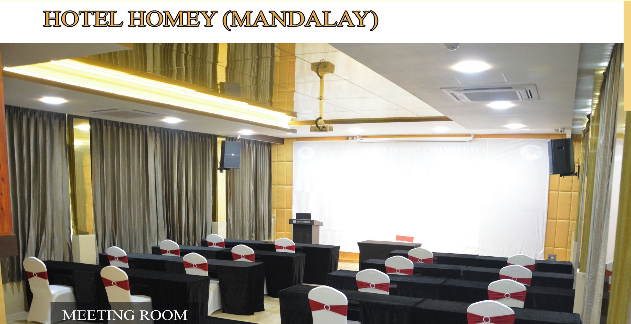 A meeting room with rows of tables and chairs, a podium, a projector, and a sound system.