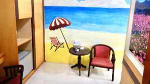 A room with a beach mural, a small round table, two chairs, and a window with a floral view. - Treehouse (Yanpu)