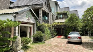 A traditional Japanese-style house with a tiled roof, a red car parked in front, and a well-maintained garden with various plants and a stone pathway. - Treehouse (Yanpu)