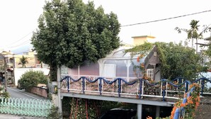 A residential area with a house featuring a balcony, a car parked in the driveway, and a garden with flowering plants. - Treehouse (Yanpu)
