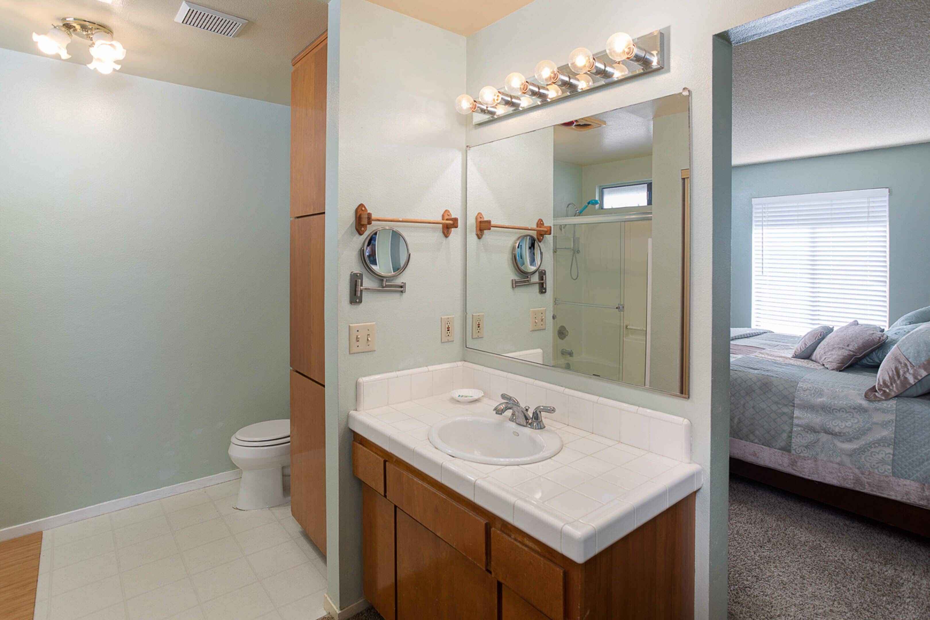 A bathroom with a white sink, wooden vanity, and a large mirror with lights.