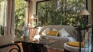 A cozy living room with a sofa, a glass coffee table, and a view of a forest through large windows. - Ground floor of beautiful villa T2 - 70 m2 - 4 people with magnificent sea views (Bastia)